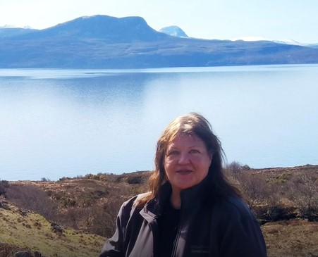 The Scottish Wildlife Trust's Crofting Officer, Anne Campbell, smiles for the camera with a loch and mountains in the background.