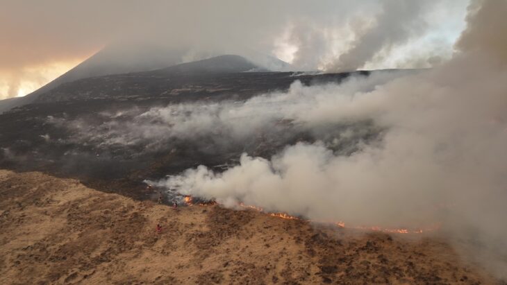 An aerial view of the mountainside of Stac Pollaidh burning, with people fighting the fire on the ground.