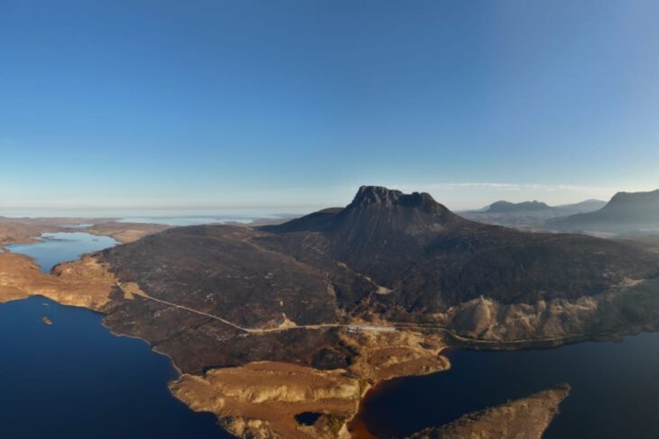An aerial view of Stac Pollaidh, its craggy summit surrounded by charred ground and a large loch.